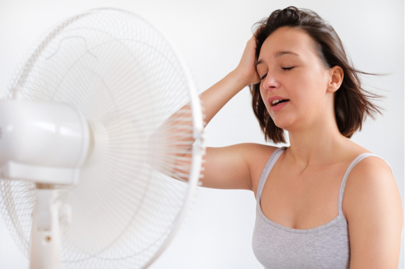 Woman without insulation trying to stay cool in front of fan.