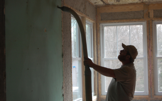 Man blowing insulation into a wall cavity with sheetrock on it