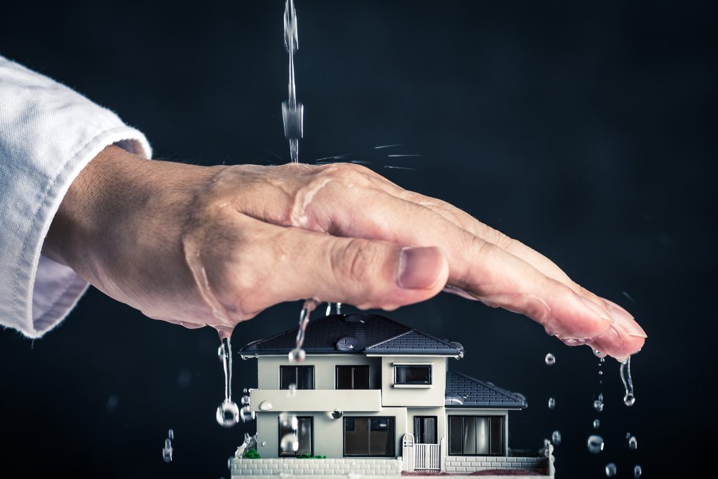 Model of a house with a hand over it to protect from pouring water