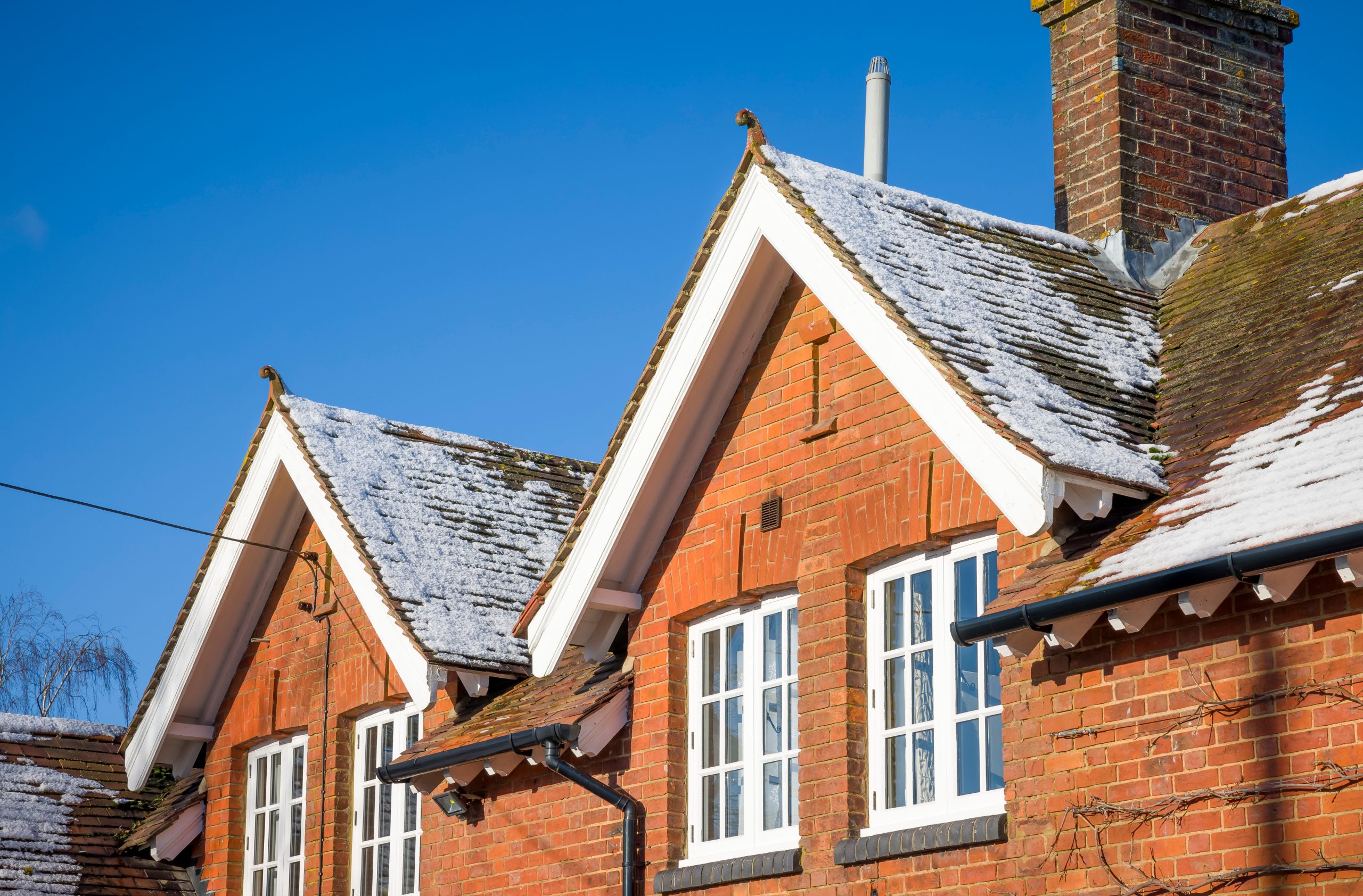 Old brick house with snow on pitched rooftop in winter