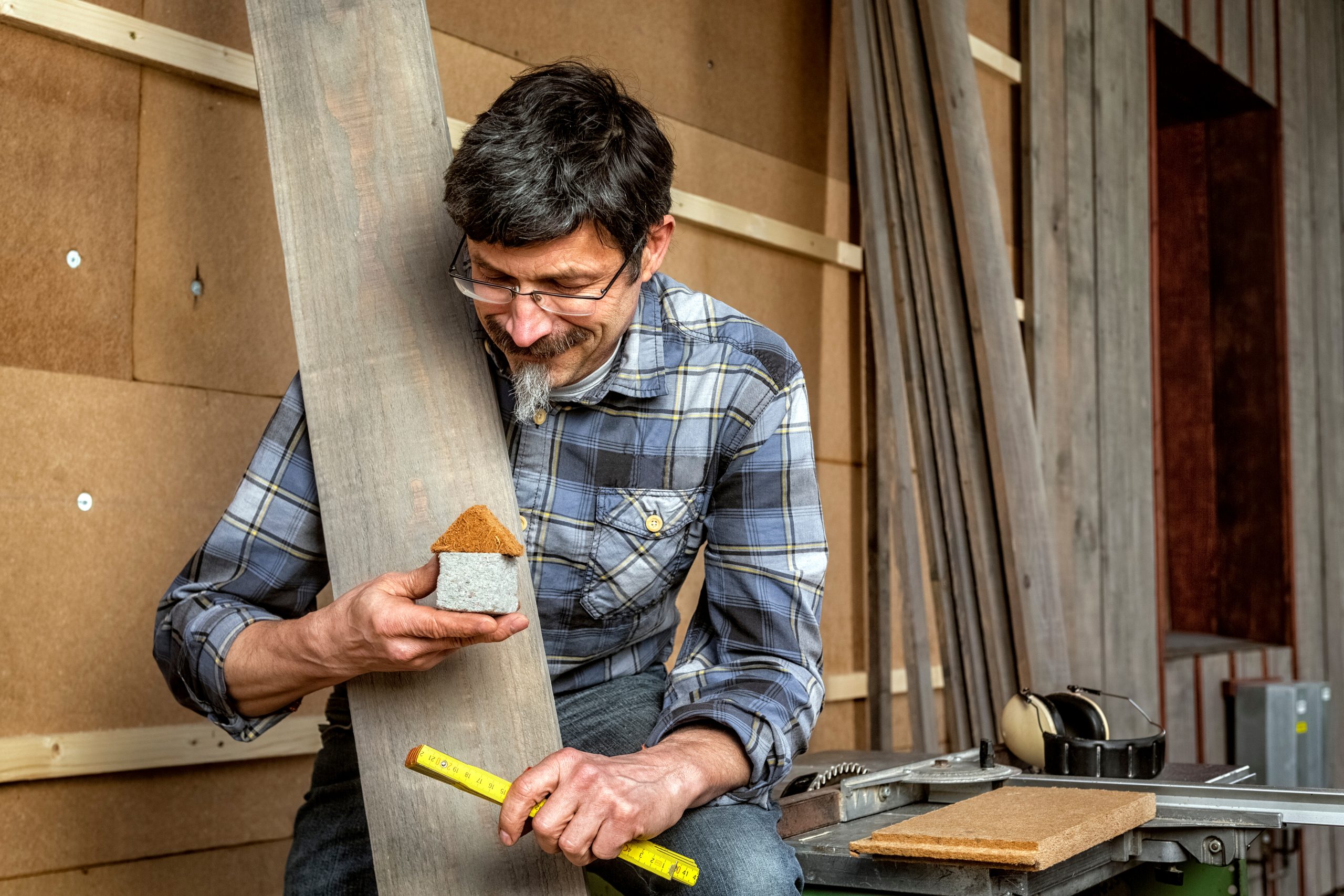 Man standing at an outer wall with insulation and a tiny home model