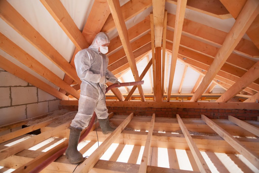 Worker with a hose spraying insulation in the attic of a house